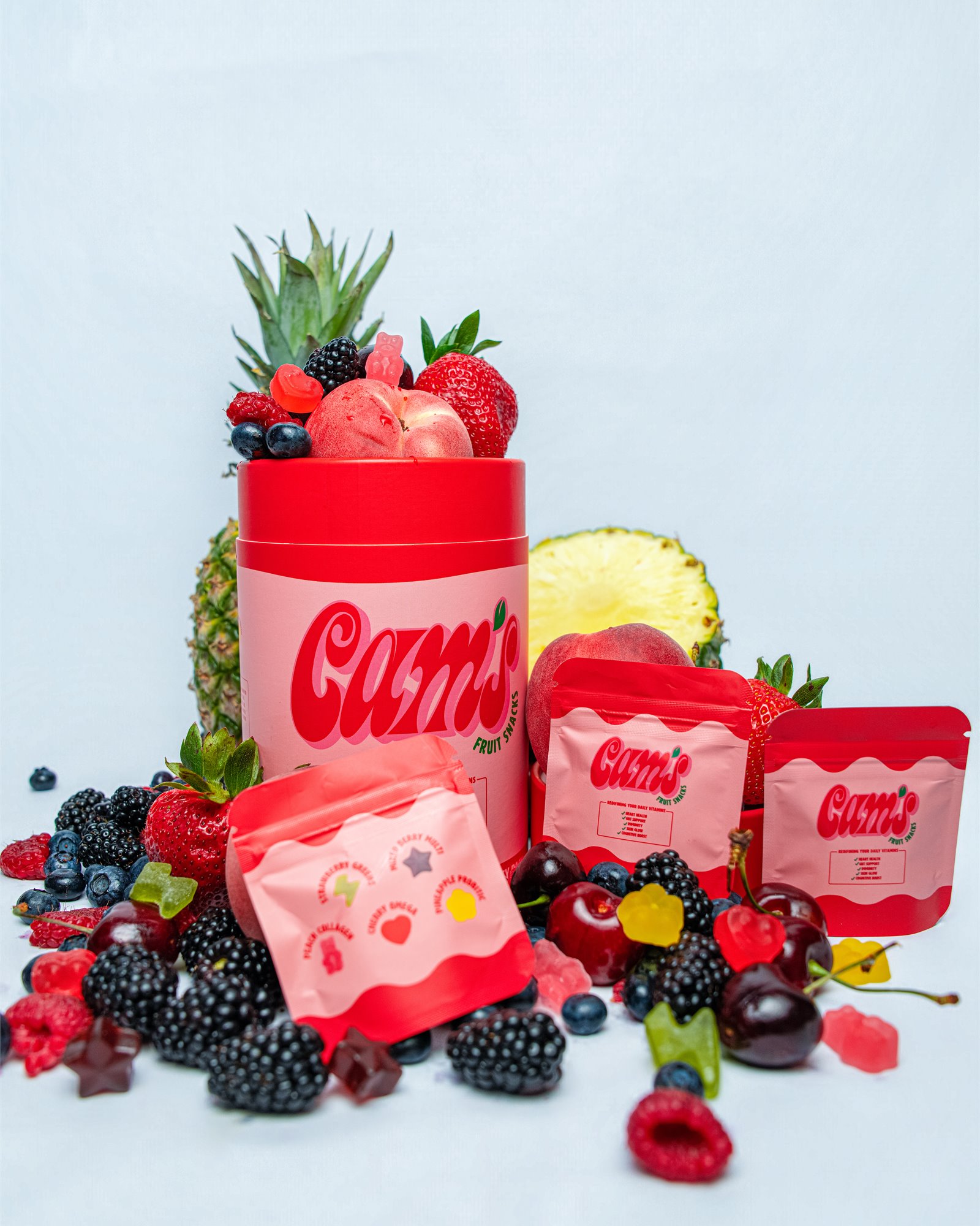 Cam's Fruit Snacks canister and pouches surrounded by fresh fruit and colorful gummies
